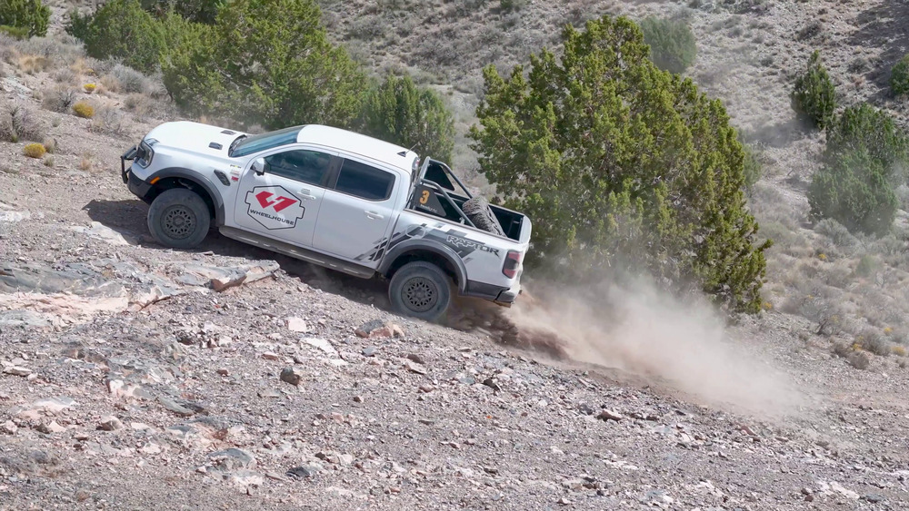 Weißer Ford Ranger Raptor klettert am Five Mile Pass einen felsigen Hang hinauf, hinter den Hinterrädern steigt Staub auf