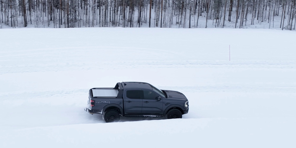 Grauer Ford Ranger Raptor fährt neben einem Wald über eine schneebedeckte Teststrecke